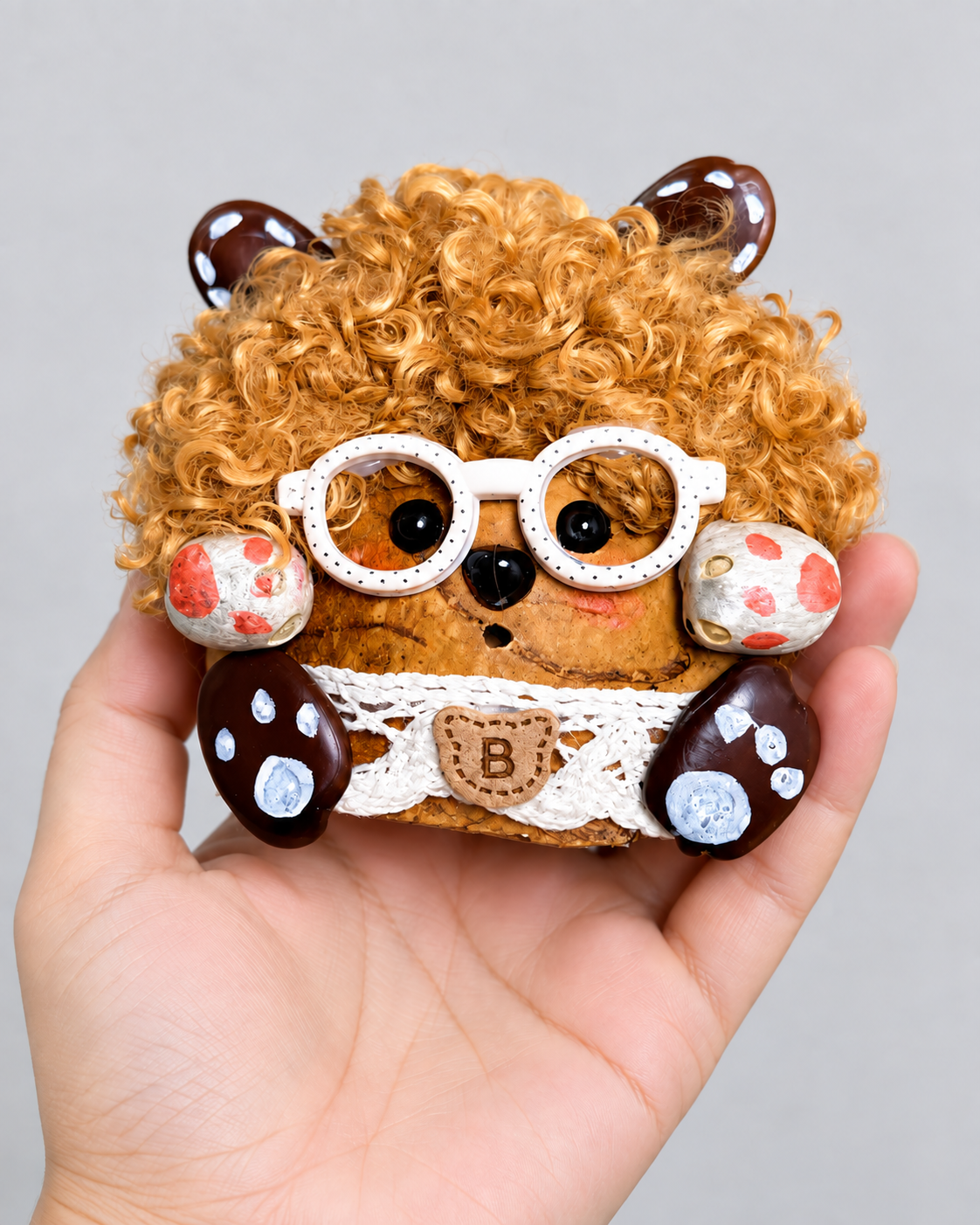 Curly handmade pod bag charm held in an adult hand to show its approximately 3.1 by 3.9 inch size