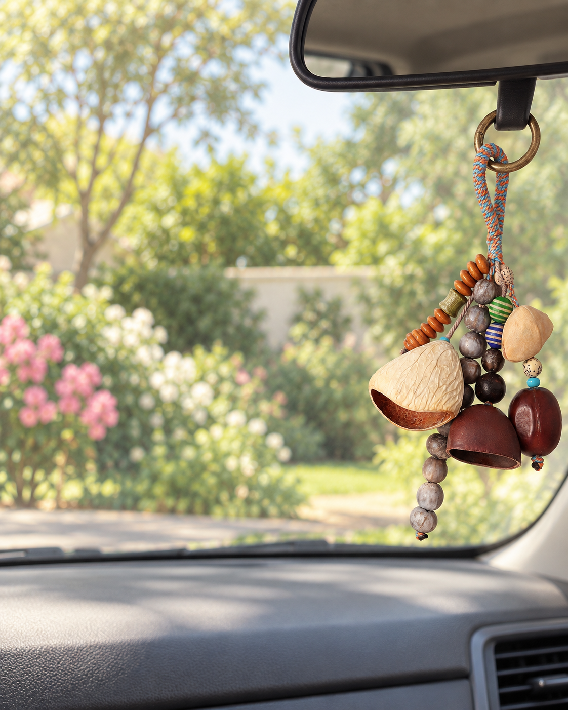 Tumble botanical shell charm hanging at the passenger-side edge of a rearview mirror in a parked car