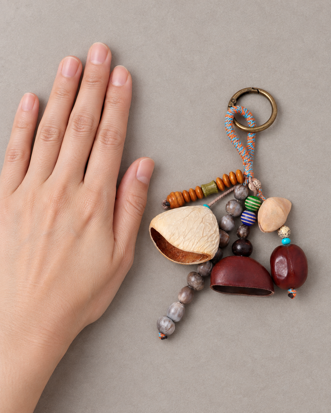 Tumble botanical shell bag charm beside an adult hand to show its approximately 5.9-inch length